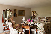 Antique cheval mirror, dressing table with armchair and bed with floral quilt in bedroom