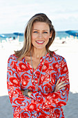 A blonde woman on a beach wearing a tunic with a floral pattern