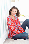 A blonde woman on a beach wearing a tunic with a floral pattern and jeans