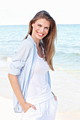 A young woman by the sea wearing a white top and a light blue shirt