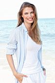 A young woman by the sea wearing a white top and a light blue shirt