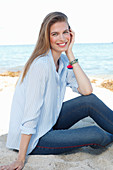 Junge Frau in hellblauem Hemd und Jeans am Meer