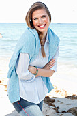 A young woman by the sea wearing a light blue shirt and jumper