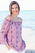 A young woman by the sea wearing a Carmen blouse