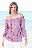 A young woman by the sea wearing a Carmen blouse and white shorts