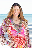 A brunette woman by the sea wearing a colourful beach dress