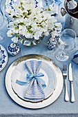 Festliches Tischgedeck mit silbernem Platzteller, blaugestreifter Serviette und Blumenstrauß