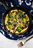A Socca Pizza with vegetables in a cast iron skillet