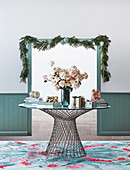 Round metal and glass table with bouquet and gifts in front of passage with Christmas garland