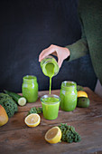 A woman pours green smoothies into glasses