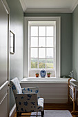 White-and-blue armchair next to bathtub below lattice window
