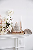White floral arrangement, paper decoration and candles on mantelpiece