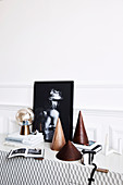 Kegelförmige Dekoobjekte, Bücher, Tischleuchte und schwarz-weiße Fotografie auf Sideboard