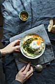 Hands holding bowl with cauliflower puree with pesto and eggs