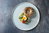 Vegetarian whole grain bagel sandwich with chopped avocado, cream cheese, sun dried tomatoes and egg