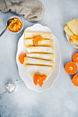Gluten free crepes served in a white oval plate, garnished with orange slices and powdered sugar