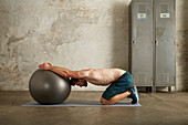 A young man performing a stretch kneeling in front of a gym ball