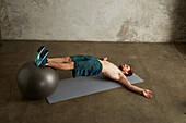 A young man lying on his back with his feet on a physio ball and buttocks raised