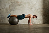 A young man doing push-ups with his legs on a physio ball