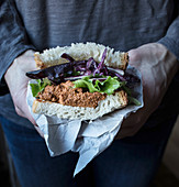 Hands holding sandwich of pate of tomatoes, fresh salad and cabbage