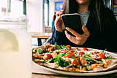 Frau mit Handy isst Salat im Restaurant