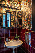 Sink in guest toilet with dark-red wall tiles and floral wallpaper