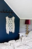 Lace waistcoat hanging from row of pegs on blue bedroom wall