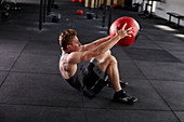 Junger Mann bei Fitnessübung Deck Squat mit Medizinball