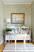 Bench, houseplant, lamp and painting on floral wallpaper in niche