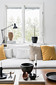 Ornaments on coffee table in front of sofa with mustard-yellow cushions below window