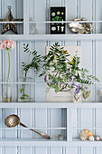 Flowers and vintage-style ornament on shelves on pale blue board wall