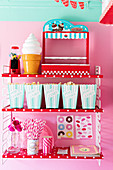 Bags of popcorn, ice-cream-shaped lamp, bubblegum machine and party utensils on red-and-white polka-dot shelves