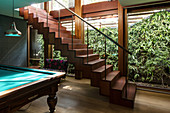 Billiard table next to self-supporting staircase in basement room with windows