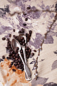 Kaffeebohnen und Löffel auf bedruckter Tischdecke