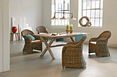Wicker armchairs around dining table in loft apartment with factory-style windows
