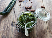 Glass jar with yummy kale pesto placed on lumber tabletop near fresh peanuts