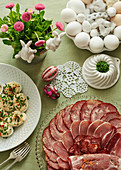 A table laid for Easter with purple Easter eggs, eggs with mayonnaise sprinkled with chives, cold cuts arranged on a glass plate