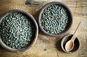 Green lentils in bowls on a rustic wooden surface