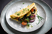 Vegan omelette (made from yellow mung beans) filled with courgette, aubergines, tomatoes and red onions
