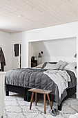 Bed in niche with sloping ceiling in bedroom in shades of grey