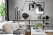 Sofa next to low shelves decorated with candles, vases and plants in grey interior