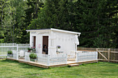 Weißes Spielhaus mit Zaun auf Podest im Garten