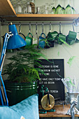 Glasses and cups on and under L-shaped shelf in corner of kitchen decorated in blue and green