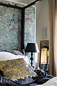 Decorative, sequinned scatter cushion on four-poster bed against partition wall