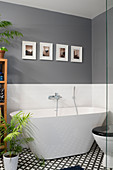 Modern free-standing bathtub in bathroom with grey walls and black-and-white tiled floor