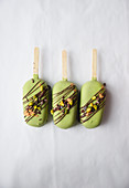 Three green ice cream sticks with pistachio nuts