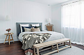 Bank vorm Bett im hellen Schlafzimmer in Weiß und Naturtönen