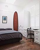 Surfboard next to the bed in the bedroom with a desk