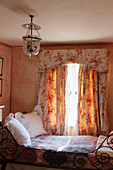 Ornate metal bed below window with toile-de-Jouy curtains and pelmet