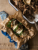 Metal bowl with delicious pulled pork and fresh bao bun placed on ornamental and linen napkins